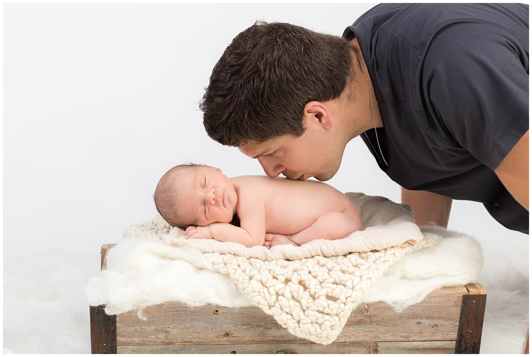 Newborn on white blankets with dad kissing