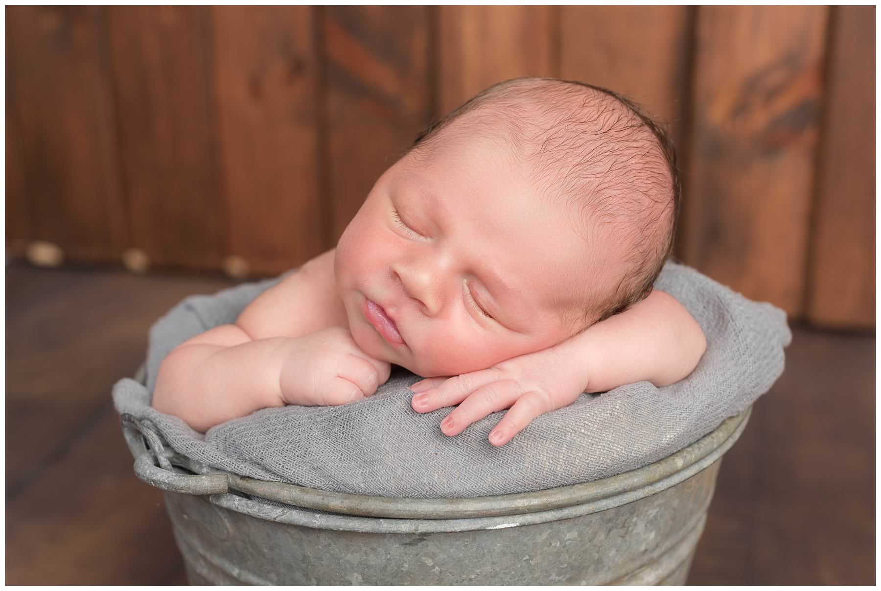 Newborn portrait in gray bucket on barn wood background