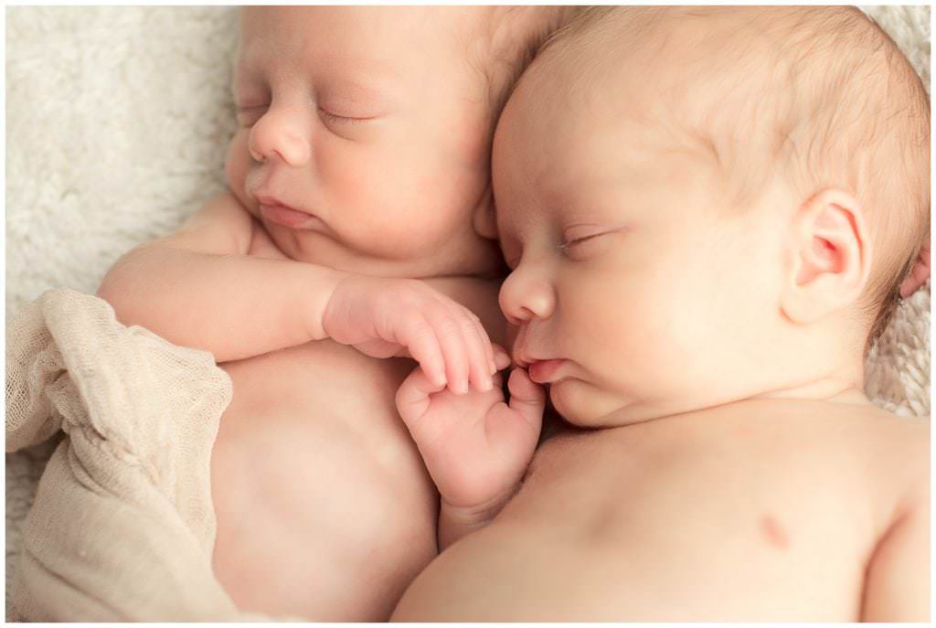 twin newborns holding hands on cream background