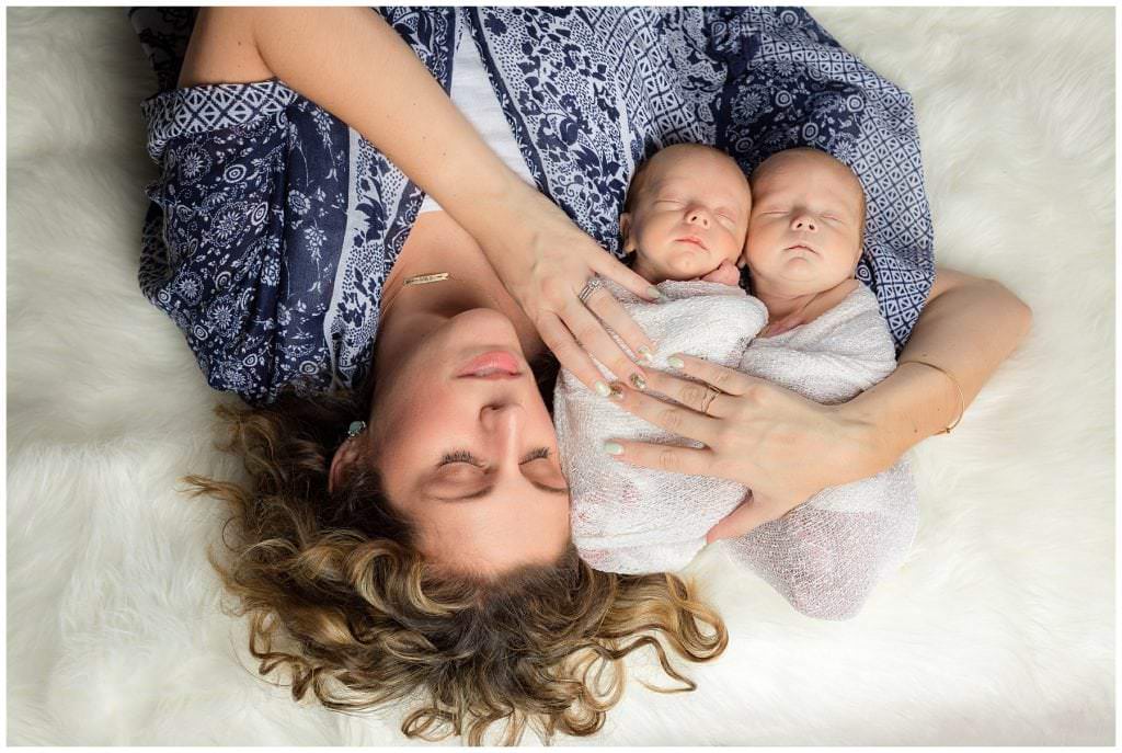 mom lying on cream rug with newborns in arm